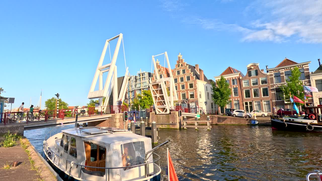 Modern drawbridge lifts for passing boats, historic Dutch architecture, bright daylight, steady wide shot