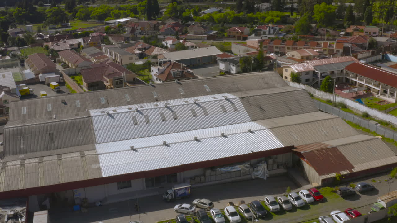Aerial shot captured with a drone showing a landscape composed of homes, a factory, mountains in the background, and large green areas.