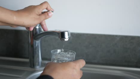 person filling a glass of water from a tap