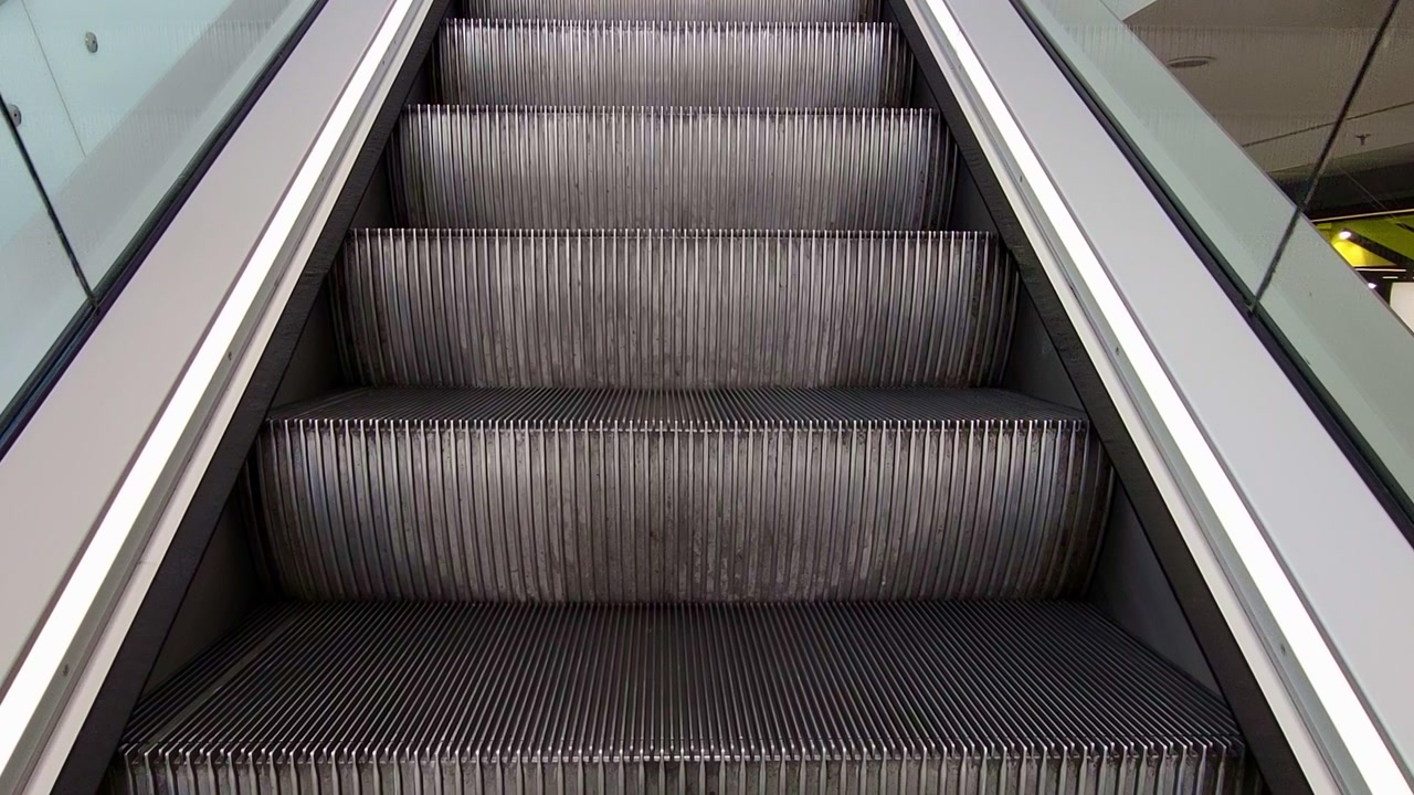 Empty escalator in operation. Shopping mall, ascending escalator in first person. Ascending on an escalator seen from the steps. Ascendingon an escalator, first-person viewpoint.