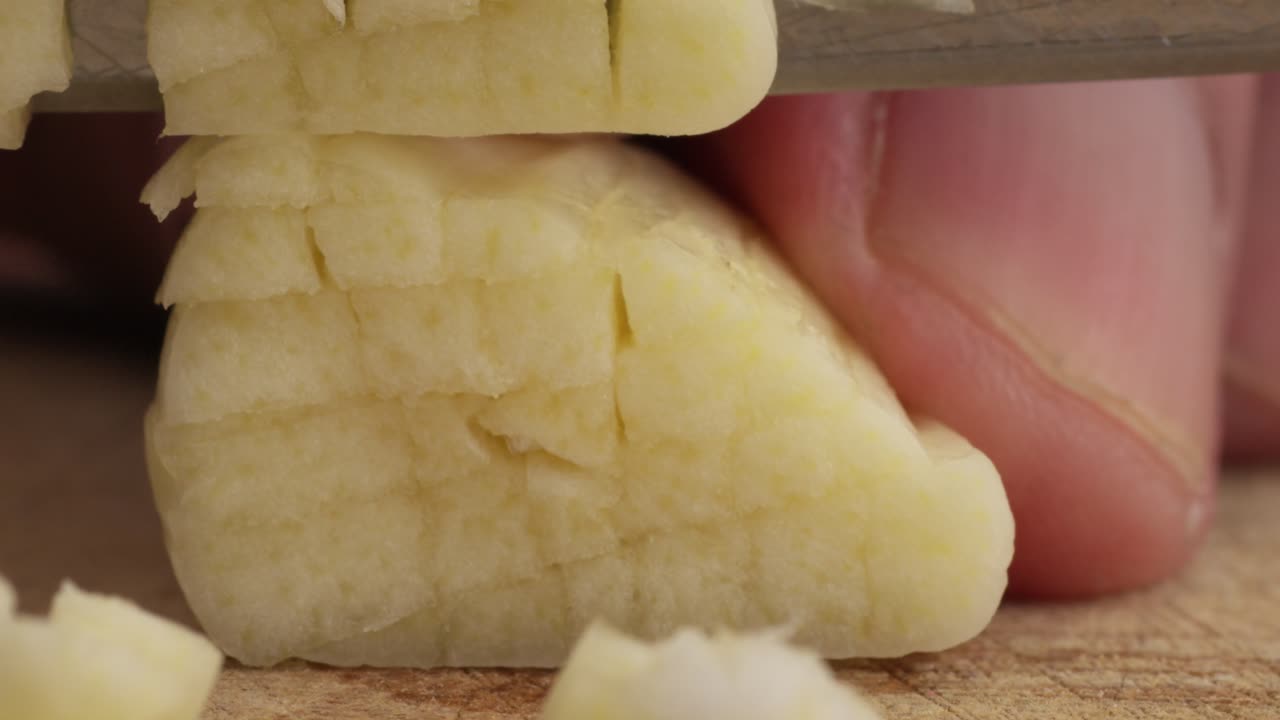 Close-up of chopping garlic with a knife on a wooden board