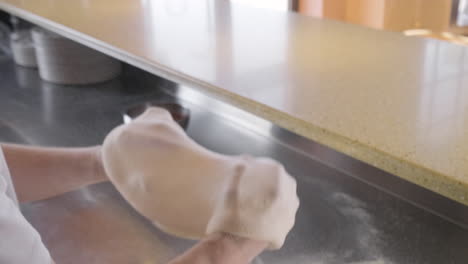 chef kneading pizza dough and waving it in the air in restaurant kitchen