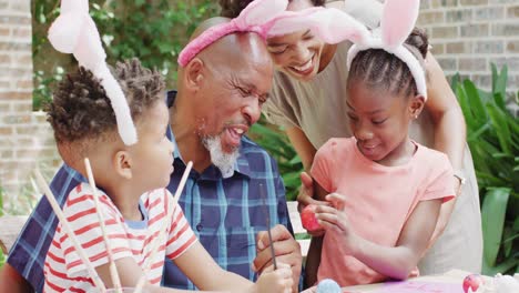 feliz hermano, hermana y madre afroamericanos pintando huevos de pascua con el abuelo, cámara lenta
