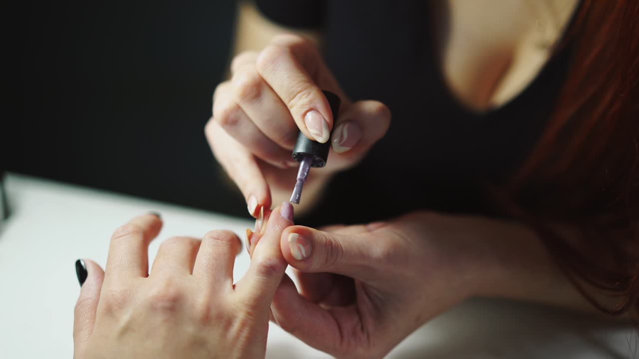 master of manicure is holding the client's finger and covering the nails with a gel polish in the beauty salon