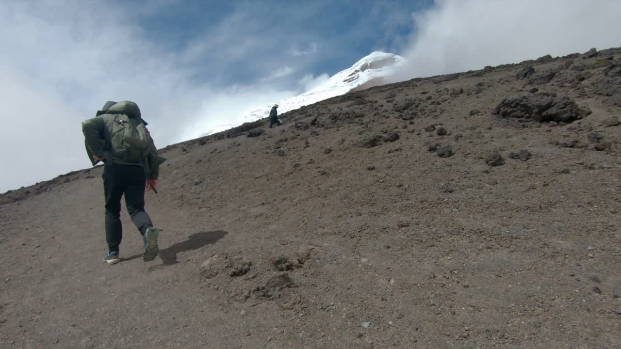 Two hikers ascends Cotopaxi volcano, Ecuador, battling against strong winds and steep inclines, slow motion