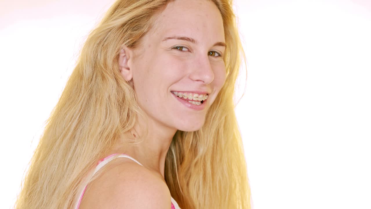 Against a white backdrop, a young blonde woman looks over her shoulder and giggles