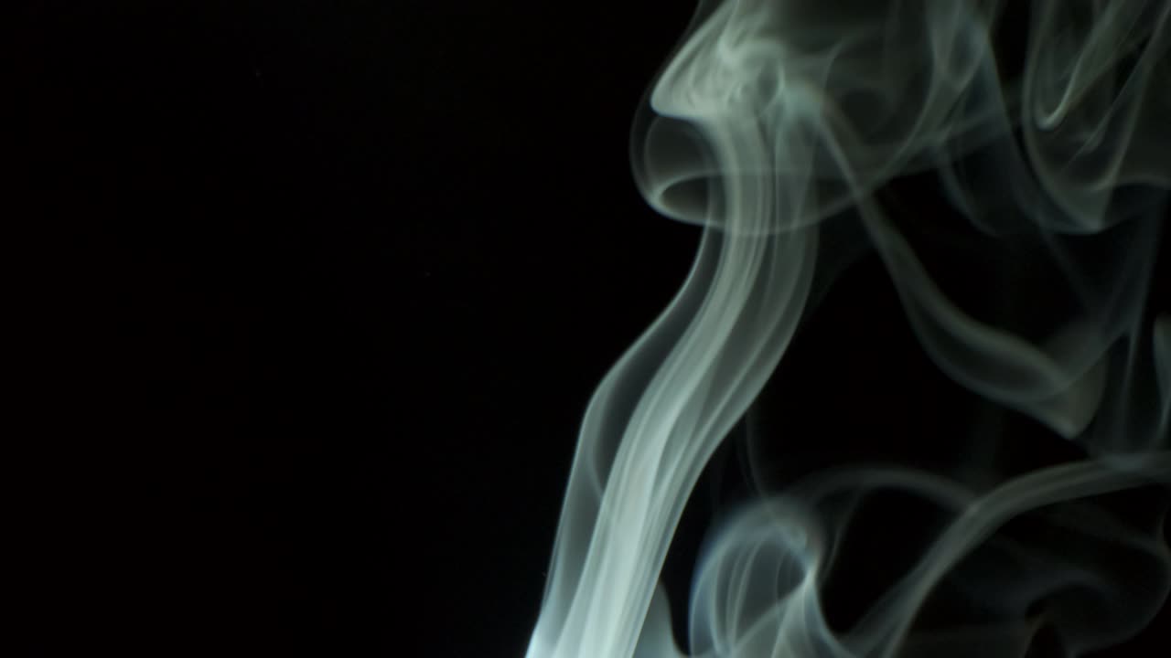 은색의 연기가 올라오고 우아하게 위로 회전합니다. 담배 연기가 아래에서 위로 불고 있습니다. 가까운, 검은 바탕에 고립되어 있습니다.
