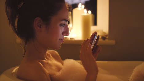 woman relaxing in a bubble bath, looking at her phone.