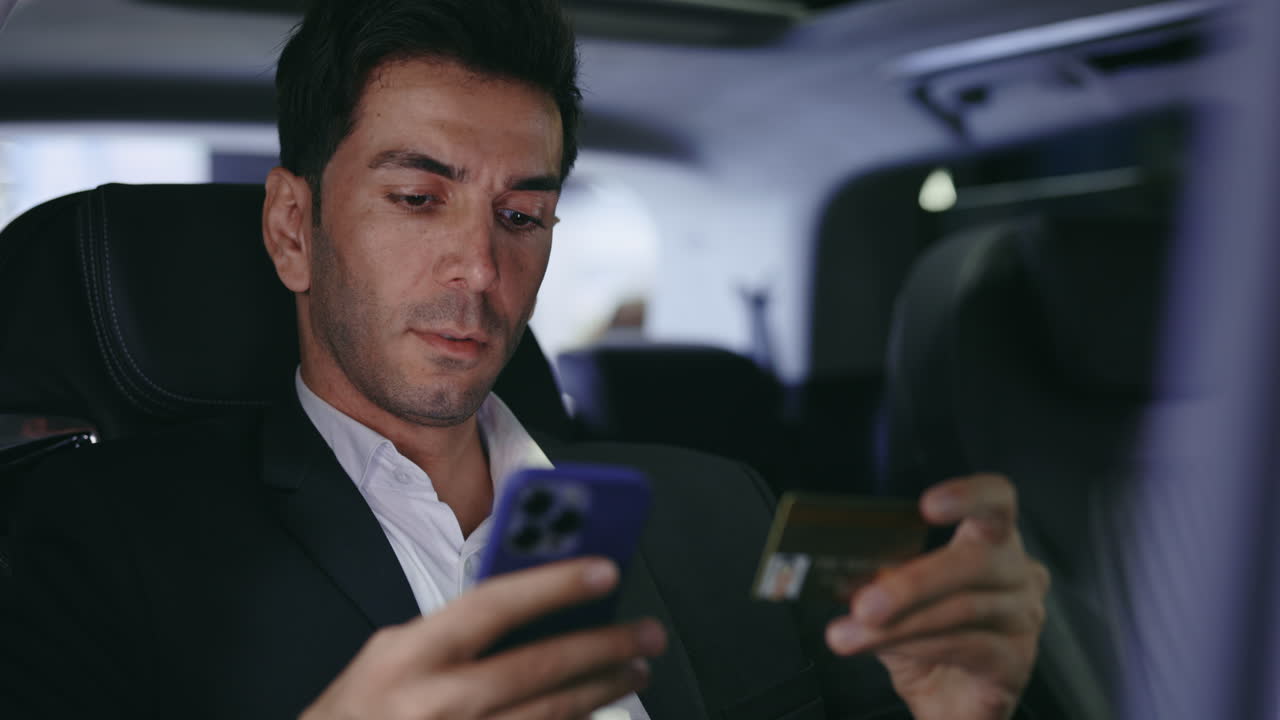 Businessman using smartphone and credit card in a car