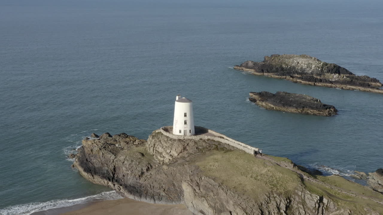 una vista aérea del faro twr mawr en la isla ynys llanddwyn, volando de izquierda a derecha alrededor del faro mientras se aleja, anglesey, norte de gales, reino unido