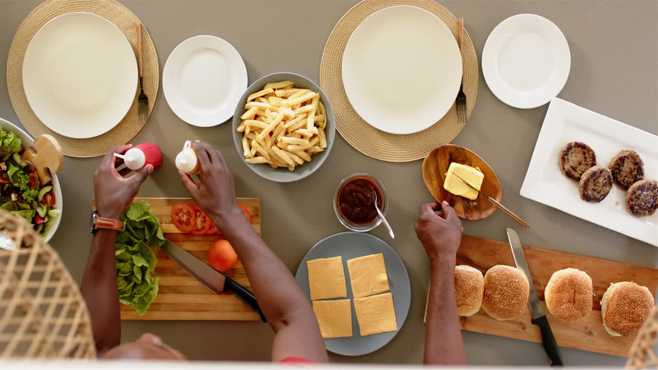 Preparing burgers with fries, person arranging ingredients on table for family meal