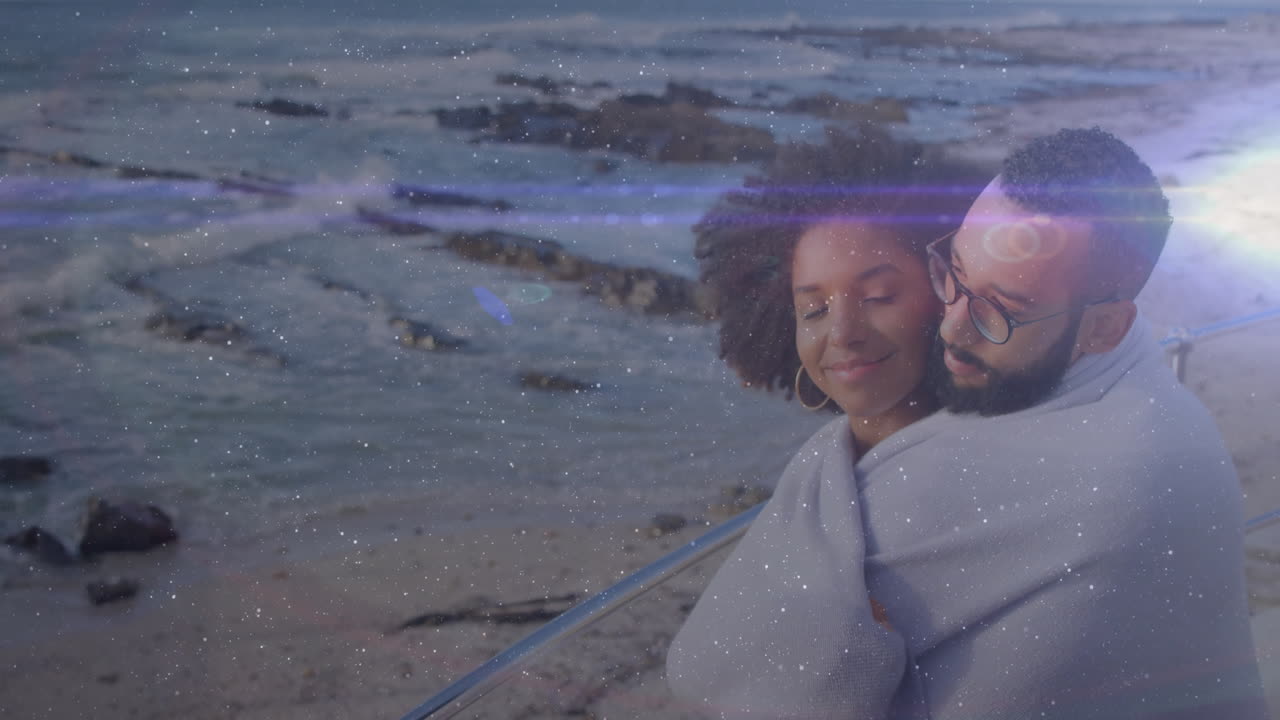 Wrapped in blanket, couple watching animation on beach with light effects
