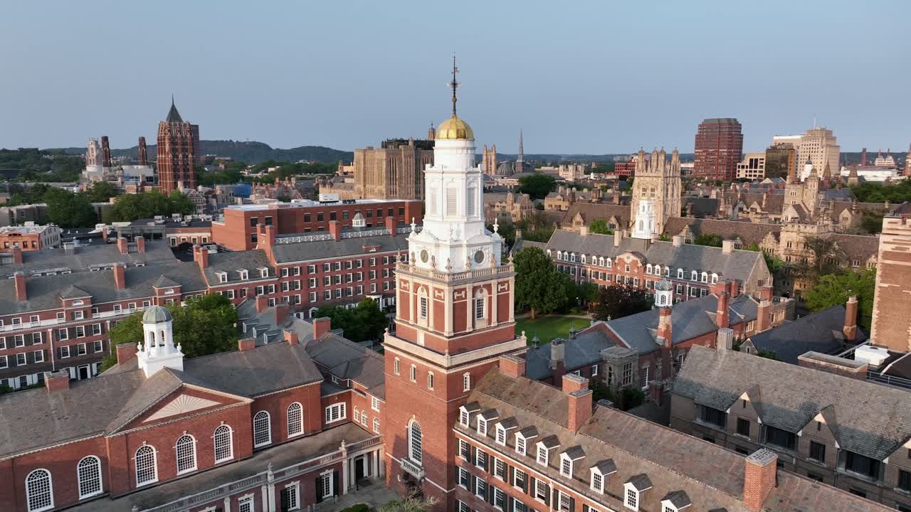 Aerial flight over Davenport college with courtyard and church tower with golden cupola. Passing by shot. Harness. Tower of Yale university in background. New Haven, Connecticut at sunset