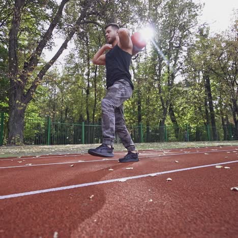 Sportsman training in the stadium. Strong athlete holding ten kg weight on back and doing his workout outdoors. Slow motion.