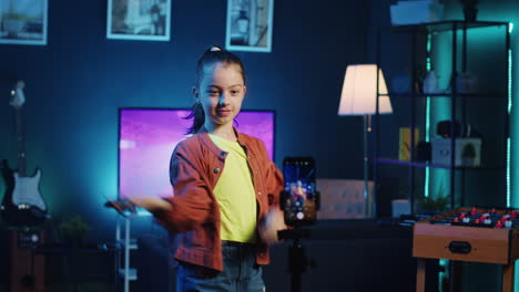 kid dancing in dimly lit home studio interior, producing content with smartphone on tripod