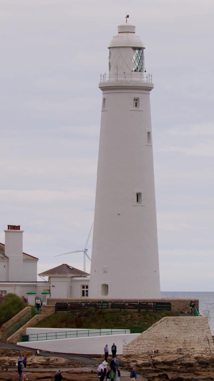 Un alto faro bianco si staglia in modo prominente contro un cielo coperto su una costa rocciosa.