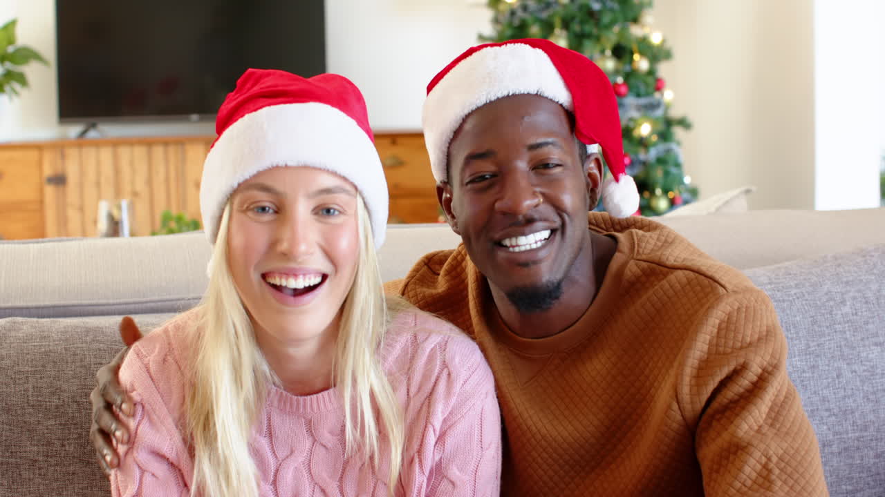 Smiling diverse couple wearing Santa hats enjoying Christmas at home together