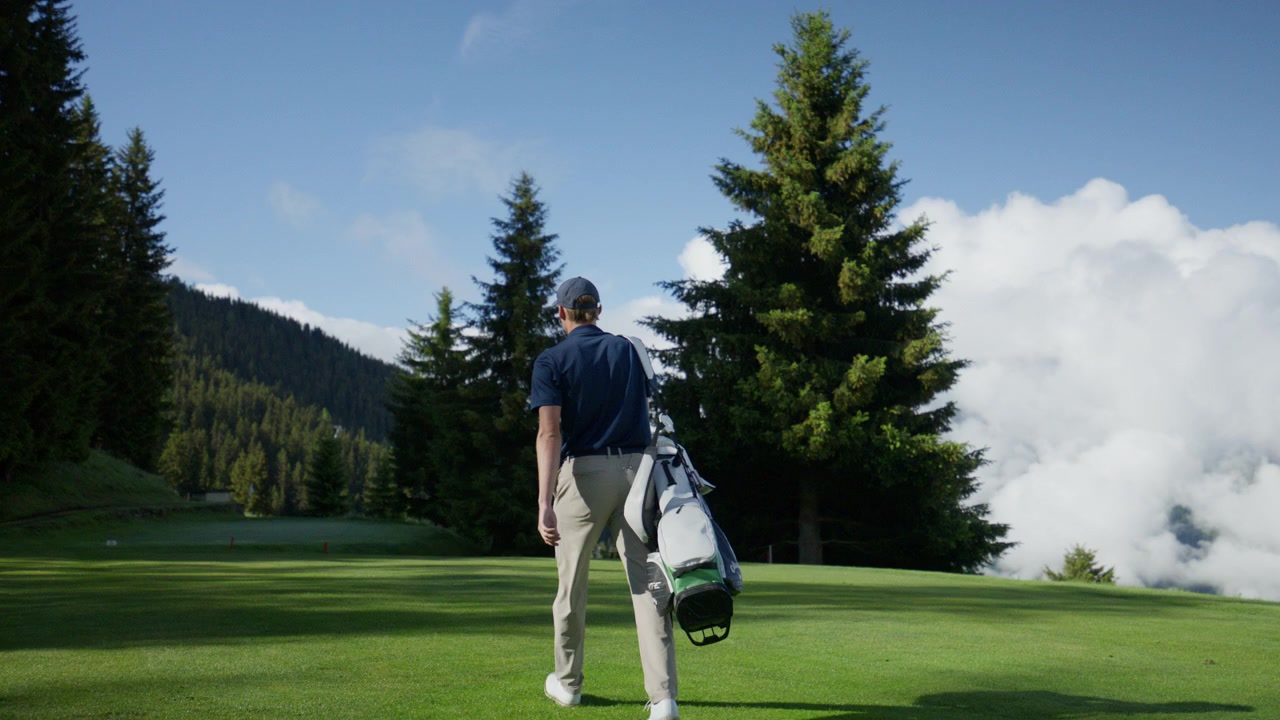 Golfista che cammina su un campo da golf alpino incontaminato portando una sacca da golf. Un paesaggio montano scenografico, pinete e nuvole spettacolari creano un'atmosfera di golf di lusso a Verbier, Svizzera