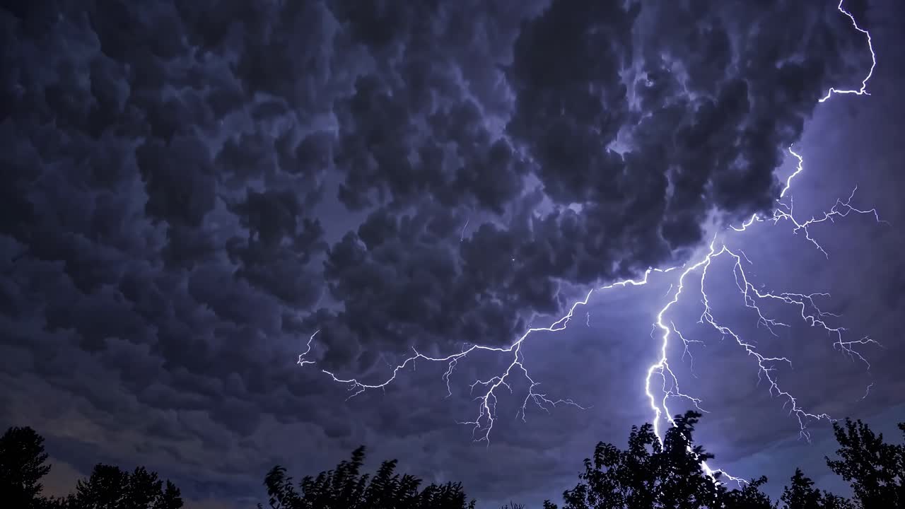 Dramatic wide-angle video of a stormy night sky with dense clouds and lightning, silhouetted trees