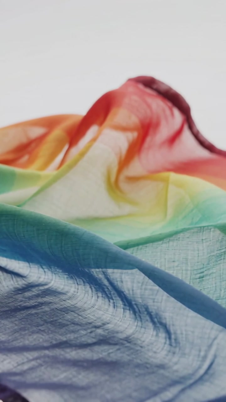 Vertical video: Rippling sheer rainbow fabric shifting ridge on white backdrop, soft breeze moving