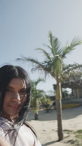 vertical video portrait of happy biracial woman smiling on sunny beach, slow motion