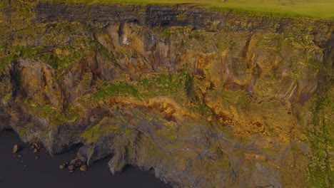 una toma aérea que revela una playa de arena volcánica negra debajo del acantilado en islandia.