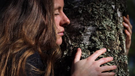 mujer natural abrazando un árbol con los ojos cerrados conectando con la naturaleza, primer plano