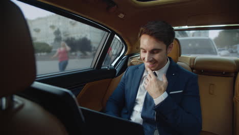 hombre de negocios sonriente hablando en una computadora portátil en un automóvil de lujo.