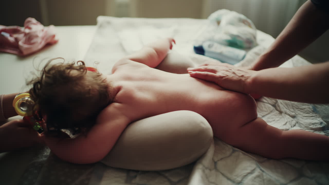 Close up of caregiver gently massaging baby's back in warm natural light