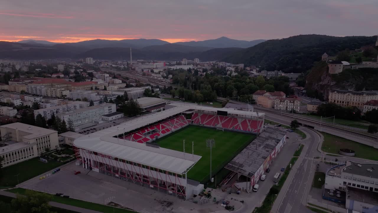 Drone shot of AS Trencin stadium glowing at sunrise with mountains, Slovakia