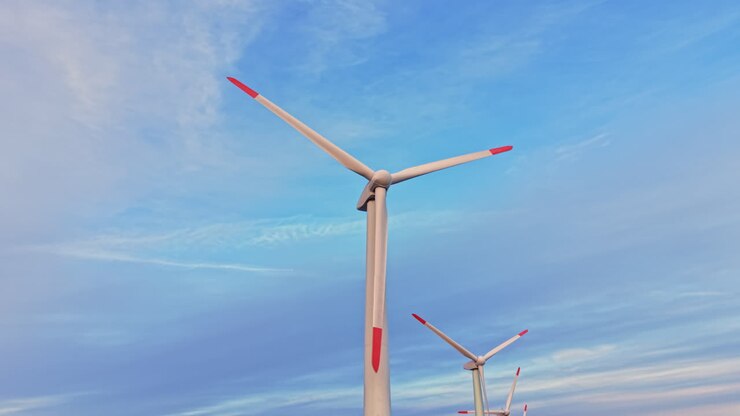 Vindmølle står højt mod den blå himmel med skyer sidst på eftermiddagen og fremhæver vedvarende energi og teknologi i bevægelse