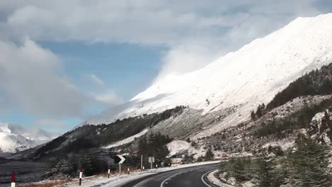 Road-trip-in-the-highlands-of-Scotland,-winter-landscape,-snowy-mountains-at-the-background,-cloudy,-traveling-shot