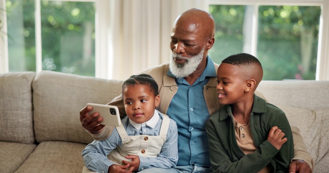 Grandfather and Grandchildren Looking at Smartphone Together on Sofa