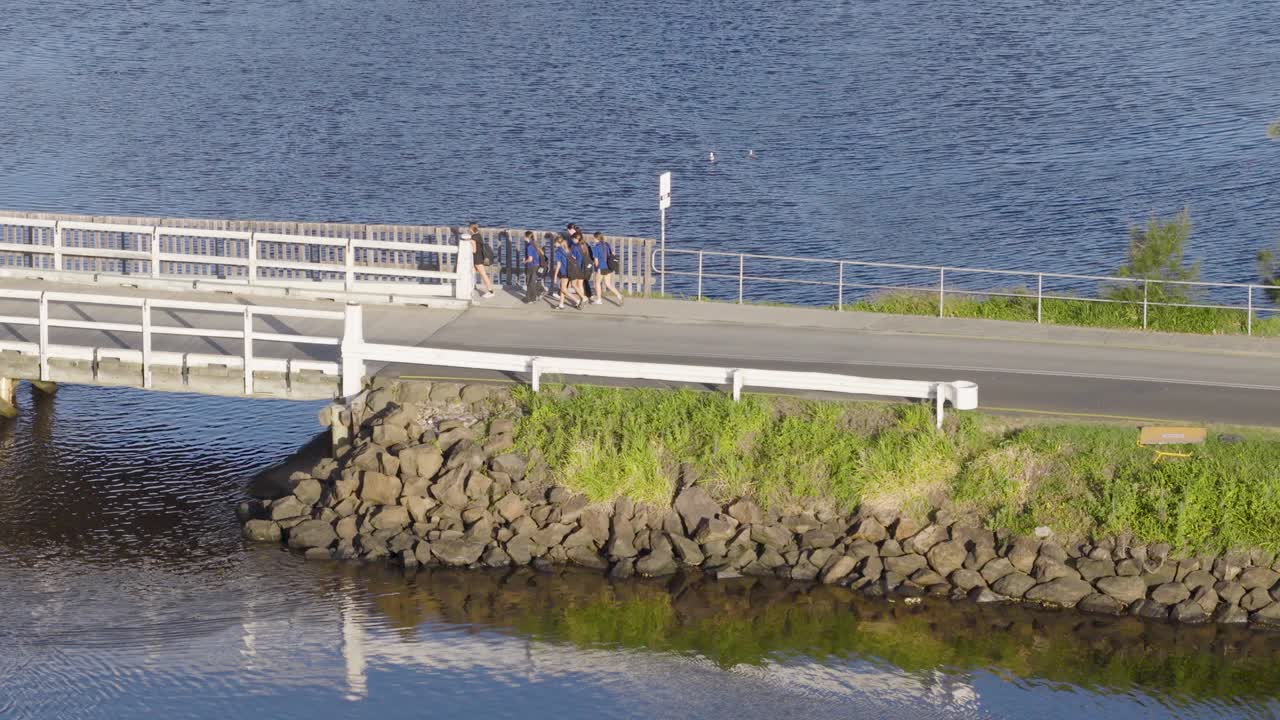 Drone footage captures a group of teens walking across a bridge in Brunswick Heads, NSW, under bright daylight