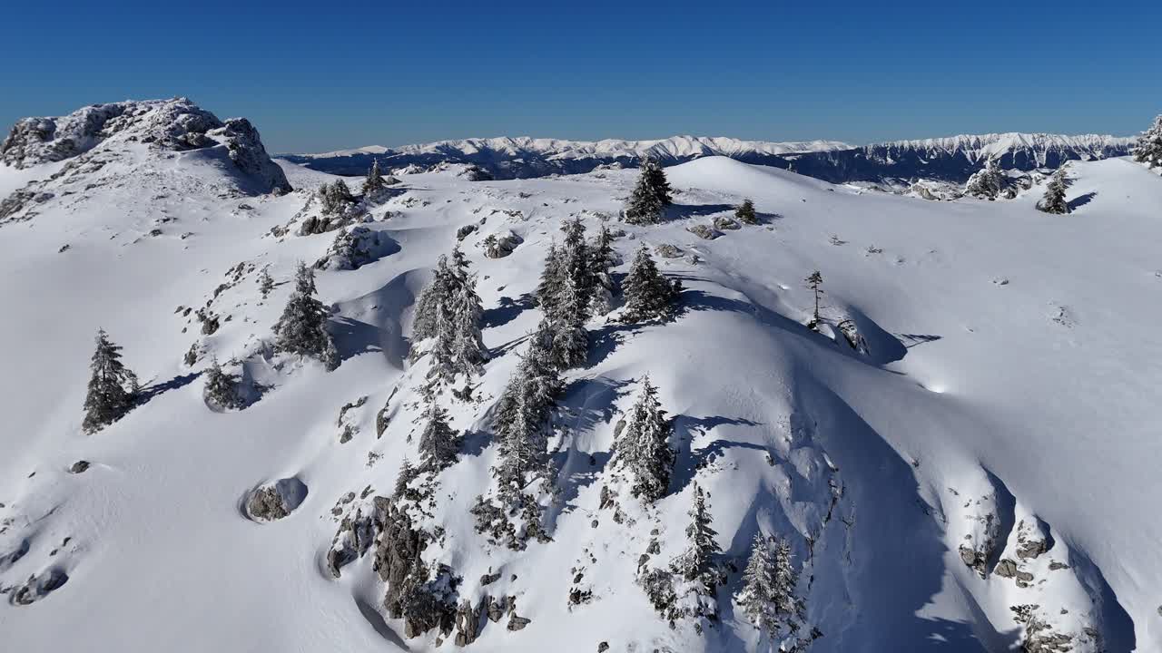 Snow-covered Bucegi Mountains under clear blue sky, rugged terrain