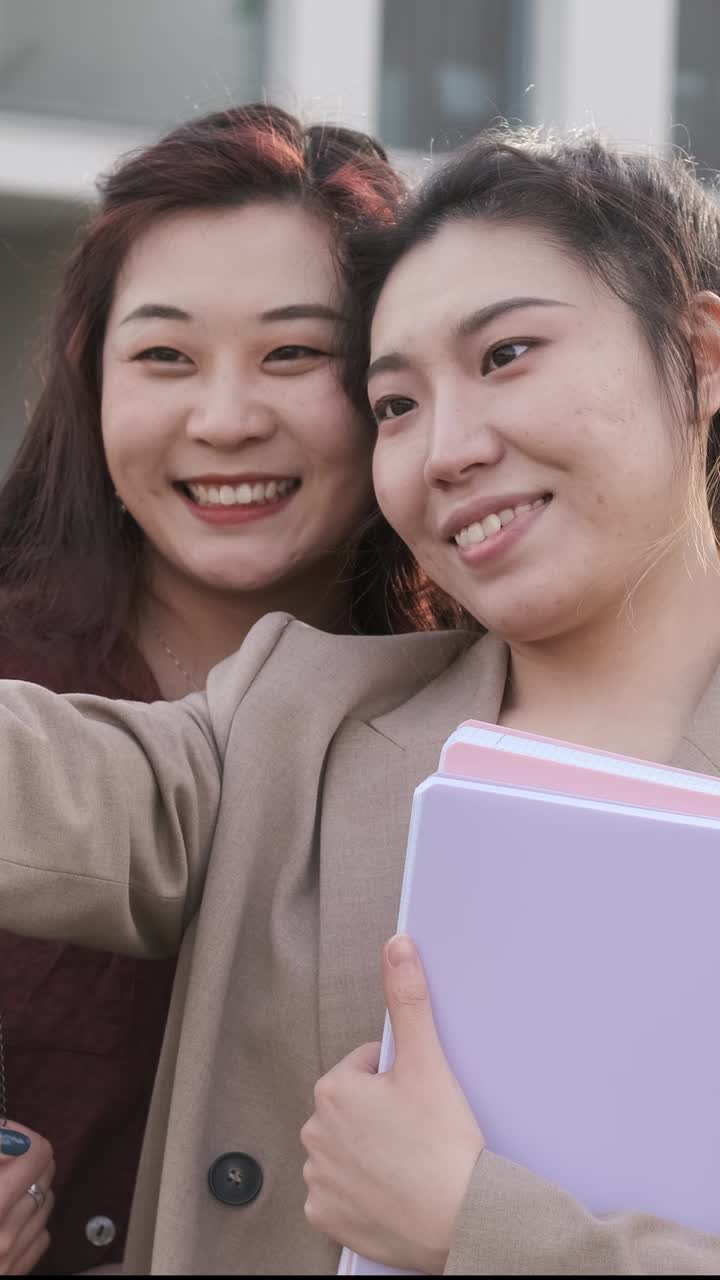 Asian college students taking a selfie with a mobile phone while standing outside the university campus. Education concept.