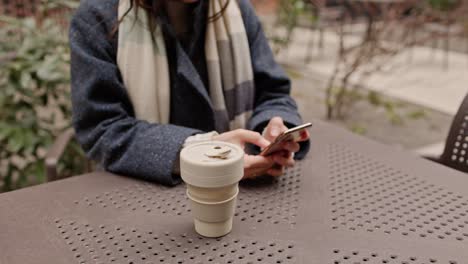 woman using phone and drinking coffee outdoors