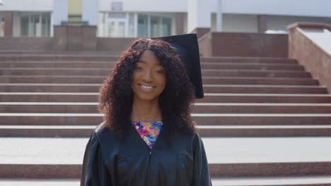 una joven afroamericana graduada se para frente a la cámara y quita una máscara médica protectora de su cara. la estudiante se para en las escaleras afuera.