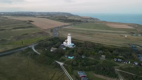 drone flying towards a little white light house during sunset, on the island of portland, dorset uk