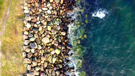 drone footage from a birds perspective flying over rocks at a coast with water splashing towards them