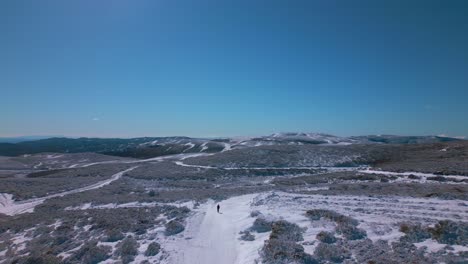 Luftaufnahme-Einer-Winterlichen-Und-Verschneiten-Landschaft-Mit-Straßen,-Bergen-Am-Horizont-Und-Einer-Person,-Die-Auf-Dem-Boden-Geht