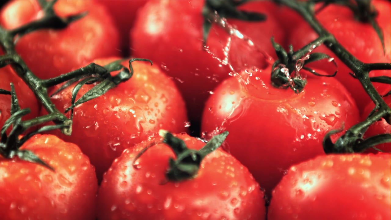 Wasser spritzt in Zeitlupe auf frische rote Kirschtomaten
