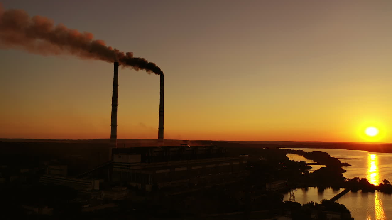Harmful emissions from factory at sunset. Dangerous smoke goes in the air from industrial plant near the river. Ecological disaster.