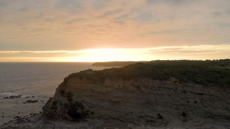 a forward moving aerial shot over big cliffs with the sunrise behind them on bass coast victoria australia