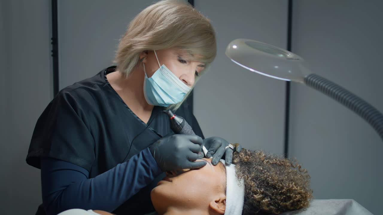 Estetista che tatua sopracciglia permanenti in uno studio di bellezza. Donna che tiene in mano la macchinetta