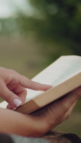 vista lateral de primer plano de una mujer sosteniendo un libro en una manta, con un fondo suavemente borroso con vegetación exuberante, capturando un momento de tranquilidad