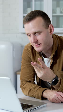 freelancer working on a laptop in kitchen. handsome guy having a video call while sitting at the kitchen table at home. student studying online. vertical video
