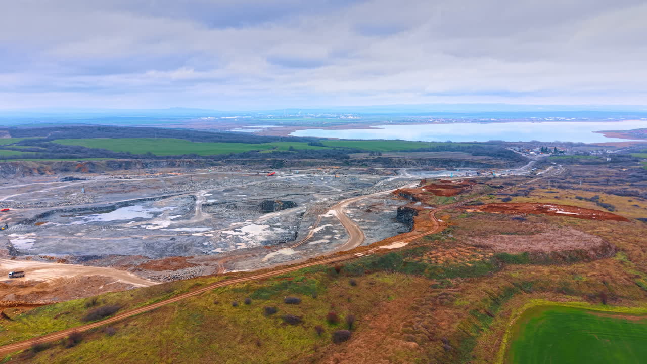 Ampia vista panoramica di una cava vicino a lago e campi. Panorama elevato che mostra una vasta area mineraria, campi agricoli verdi, un grande specchio d'acqua e una cittadina lontana.