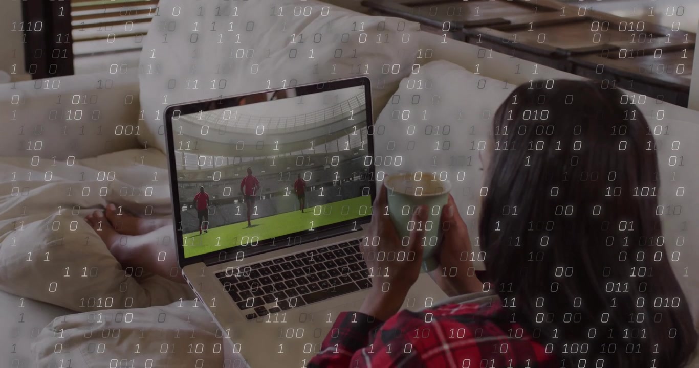 Mulher se acomodando no sofá, tomando um gole de uma caneca e ajustando o laptop para assistir a uma partida de esportes com sobreposição binária