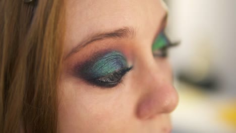 close up of young female model is being maked up in studio. artist is applying black liner to lower lid of the right eye using a brush. side view